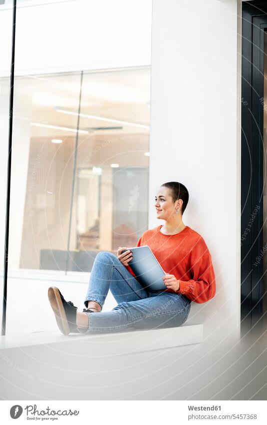 Relaxed businesswoman sitting on windowsill in office building, using digital tablet Occupation Work job jobs profession professional occupation business life