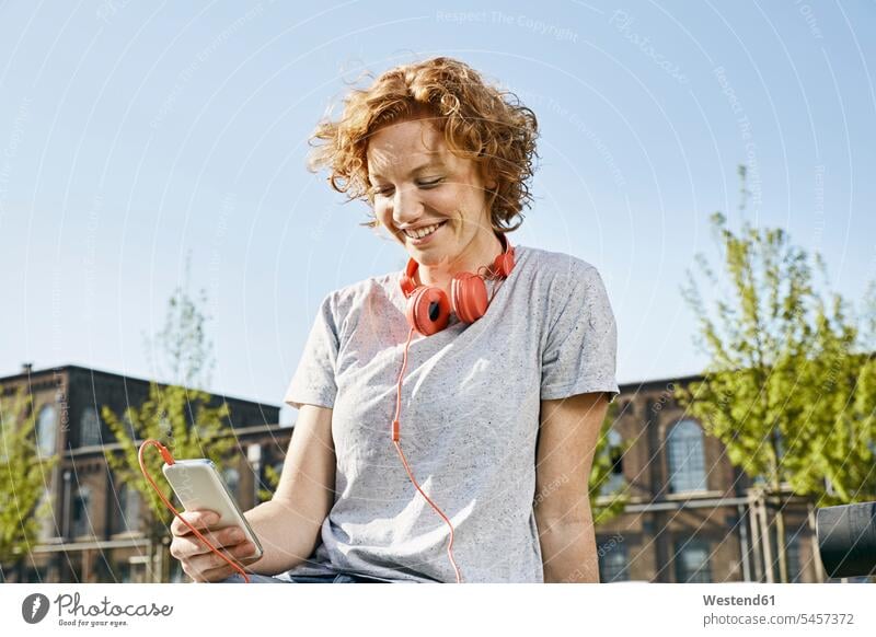 Smiling young woman with headphones using smartphone in urban surrounding urbanity headset smiling smile Smartphone iPhone Smartphones females women urban scene