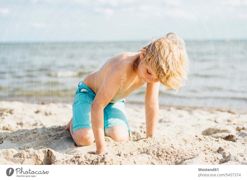Blond boy playing with sand on the beach boys males sandy beaches blond blond hair blonde hair child children kid kids people persons human being humans