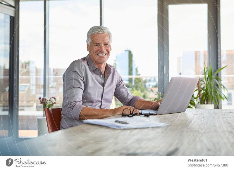Portrait of smiling mature man using laptop on table at home Laptop Computers laptops notebook portrait portraits men males smile Table Tables computer