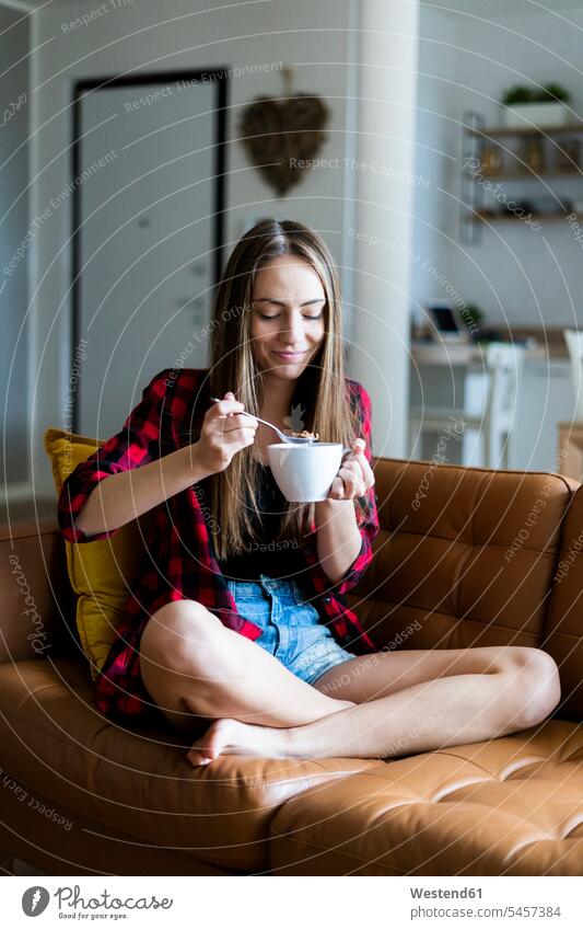 Relaxed young woman eating cereals in living room at home human human being human beings humans person persons celibate celibates singles solitary people