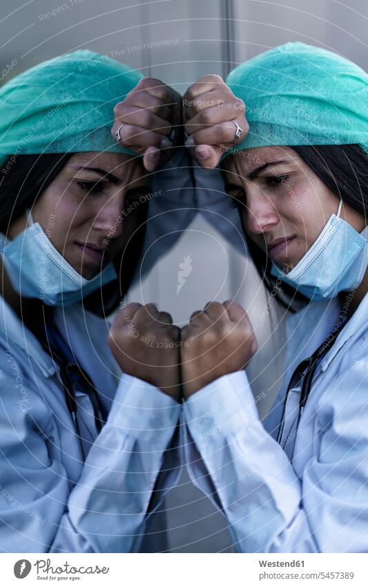Sad doctor wearing face mask leaning on glass wall of hospital color image colour image outdoors location shots outdoor shot outdoor shots day daylight shot