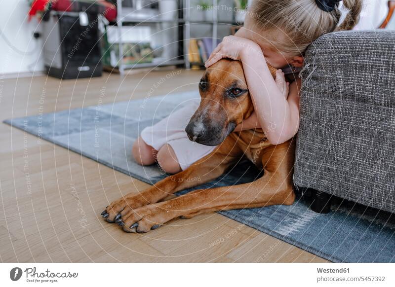 Girl embracing dog while relaxing on carpet in living room at home color image colour image Germany Home Interior Home Interiors domestic space livingroom