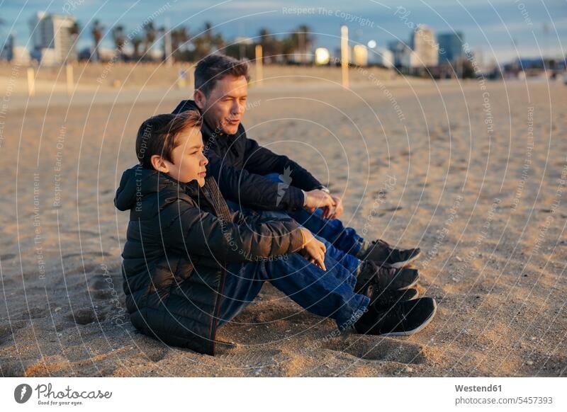 Father and son sitting on the beach beaches Seated sons manchild manchildren father pa fathers daddy dads papa family families people persons human being humans
