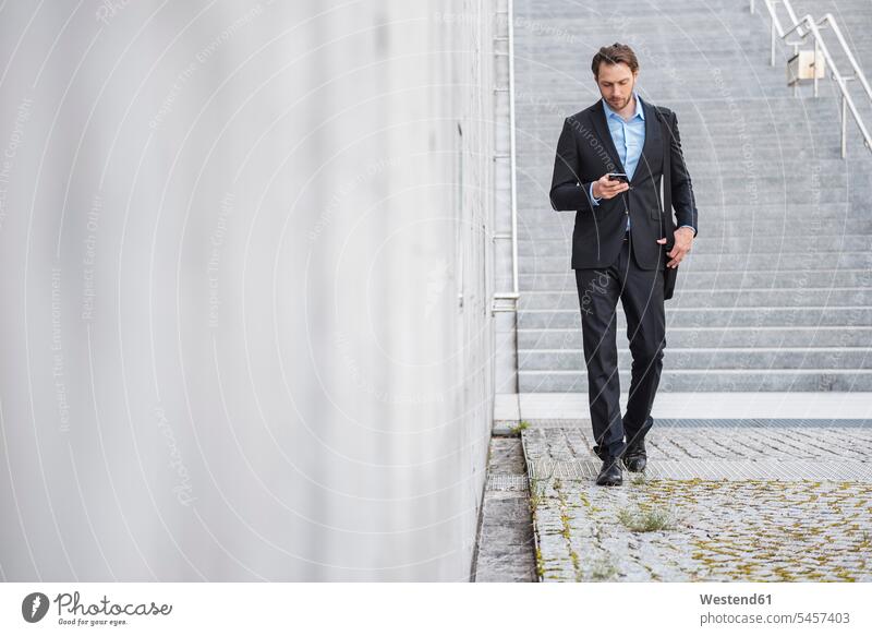 Businessman walking at stairs looking at smartphone Smartphone iPhone Smartphones stairway Business man Businessmen Business men mobile phone mobiles