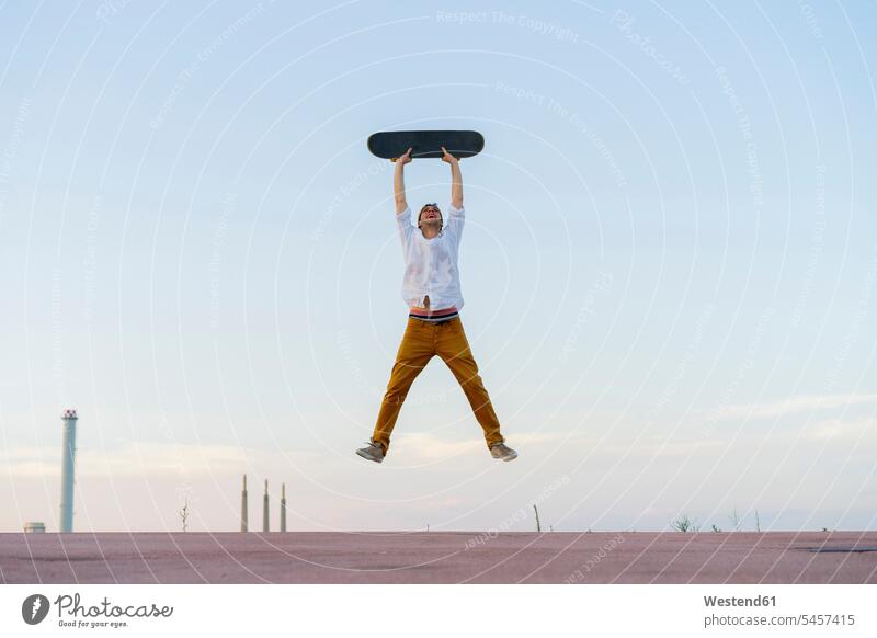 Young man jumping in the air holding a skateboard Leaping Skate Board skateboards men males jumps Adults grown-ups grownups adult people persons human being