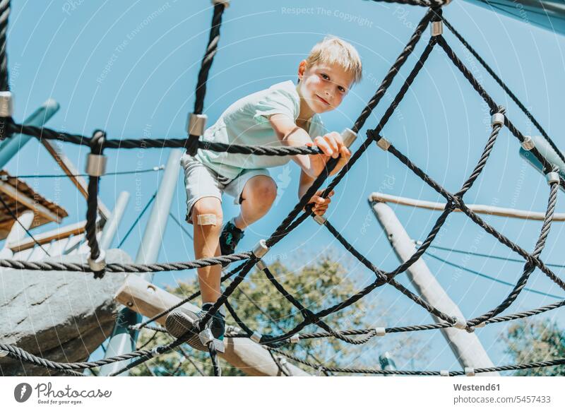 Boy climbing on spider web in public park during sunny day color image colour image outdoors location shots outdoor shot outdoor shots daylight shot
