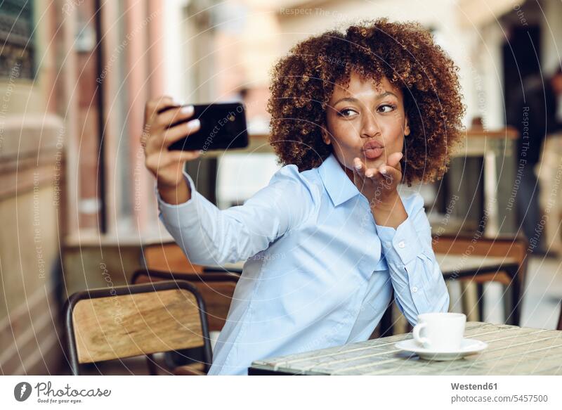 Woman with afro hairstyle sitting in outdoor cafe taking a selfie Selfie Selfies Afro Afros woman females women smiling smile Seated people persons human being
