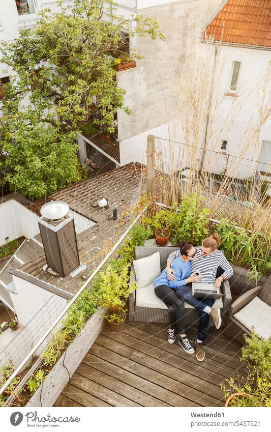 Young couple relaxing on their balcony couch settee sofa sofas couches settees using laptop using a laptop Using Laptops balconies twosomes partnership couples