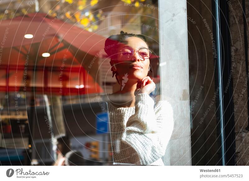 Confident young woman wearing eyeglasses looking through window at cafe color image colour image Spain outdoors location shots outdoor shot outdoor shots day