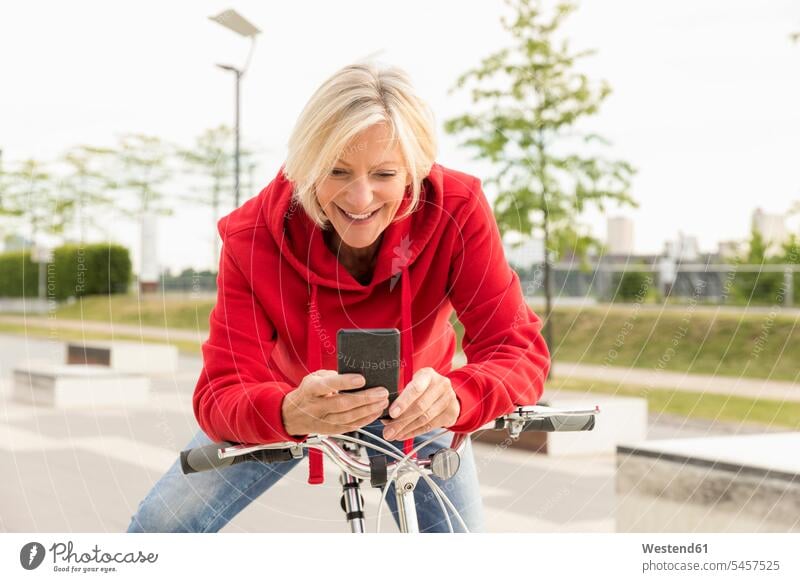 Smiling senior woman with city bike using cell phone bicycle bikes bicycles smiling smile confidence confident mobile phone mobiles mobile phones Cellphone