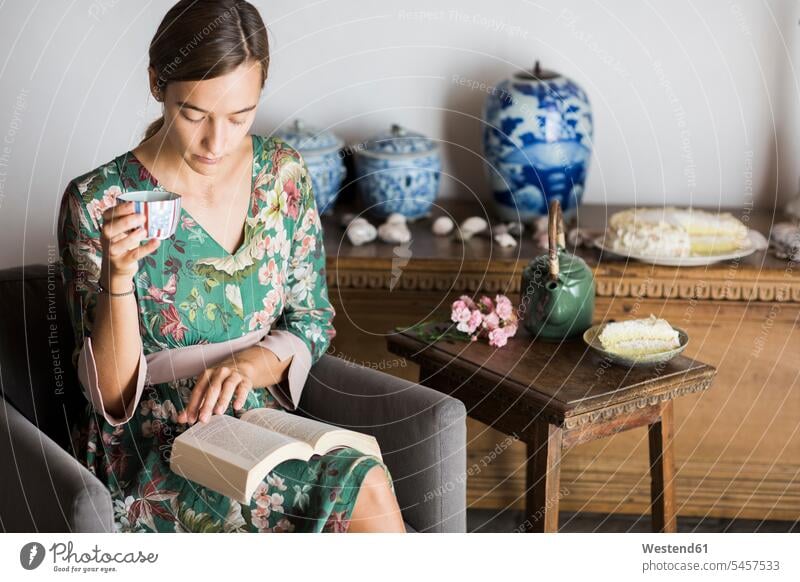 Young woman drinking cup of tea while reading a book at home books females women Tea Teas Adults grown-ups grownups adult people persons human being humans