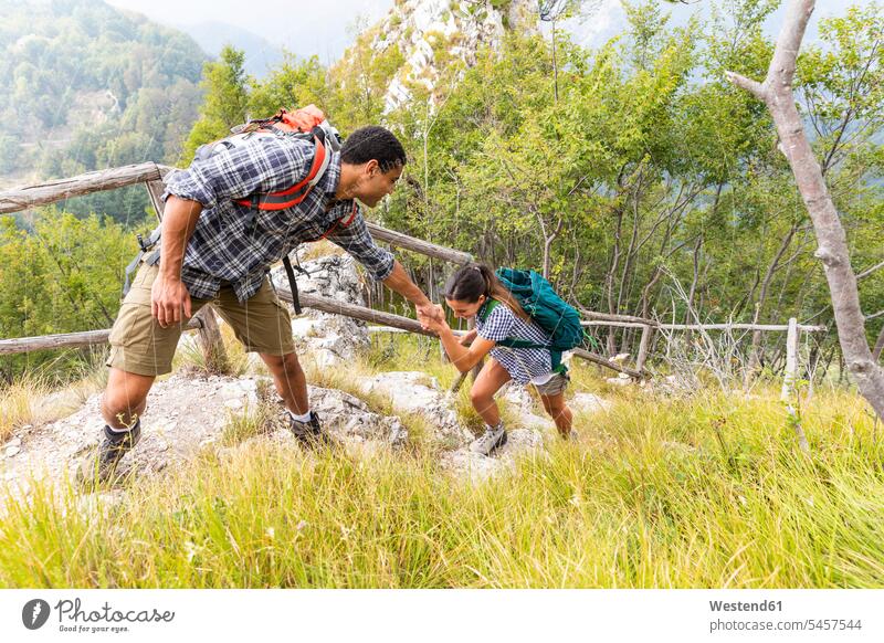 Italy, Massa, man helping a young woman to climb a step while hiking in the Alpi Apuane mountains assistance assisting Help mountain range mountain ranges hike