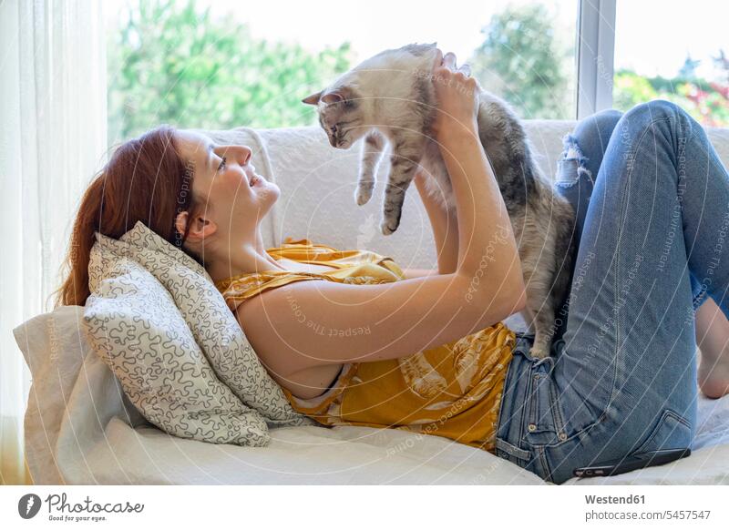 Young woman lying on the couch at home holding her cat human human being human beings humans person persons celibate celibates singles solitary people