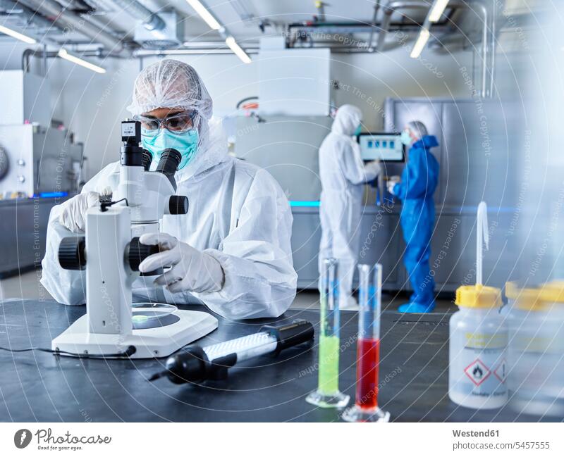 Chemists working in industrial laboratory, wearing protective clothing, using microscope Protective Suit chemist At Work Chemical Laboratory sterile clothing