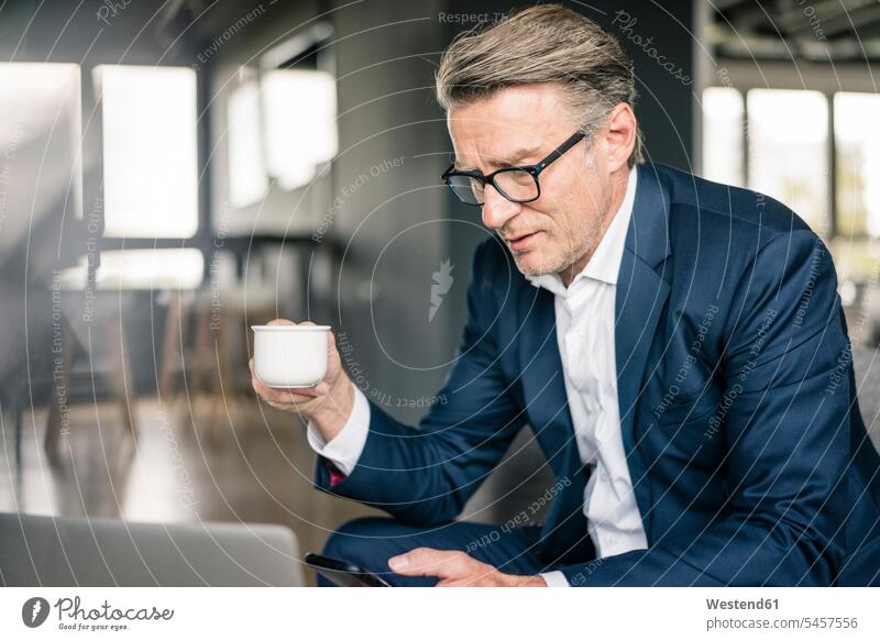 Mature businessman with cup of coffee and laptop using cell phone Coffee mobile phone mobiles mobile phones Cellphone cell phones Coffee Cup Coffee Cups