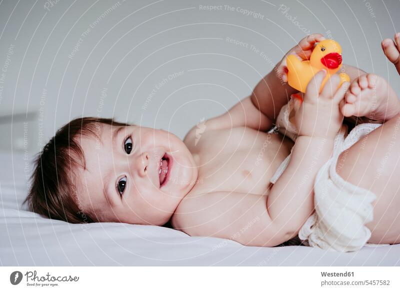 Smiling cute baby boy playing with duck toy while lying down on bed at home color image colour image indoors indoor shot indoor shots interior interior view