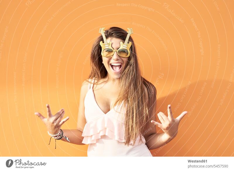 Portrait of smiling young woman with guitar sunglasses in front of orange background females women screaming shouting portrait portraits guitars sun glasses