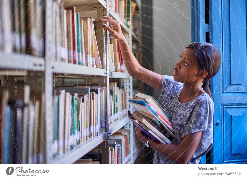 Young woman checking the books at the bookshelves at National library, Maputo, Mocambique rack racks Shelve book shelf Book Shelves learn read study stand