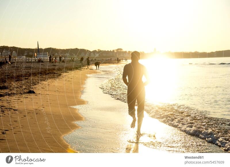 Man jogging at the beach at sunset running jogger joggers rear view back view view from the back sunsets sundown beaches man men males athlete Sportspeople