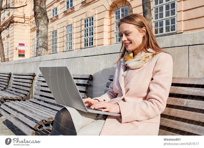Austria, Vienna, smiling young woman sitting on bench at MuseumsQuartier using laptop females women Museumsquartier MQ Seated Laptop Computers laptops notebook