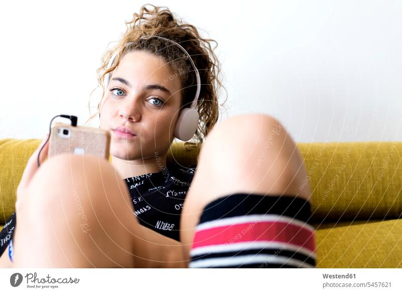 Portrait of girl sitting on the couch listening music with headphones and smartphone settee sofa sofas couches settees Smartphone iPhone Smartphones females