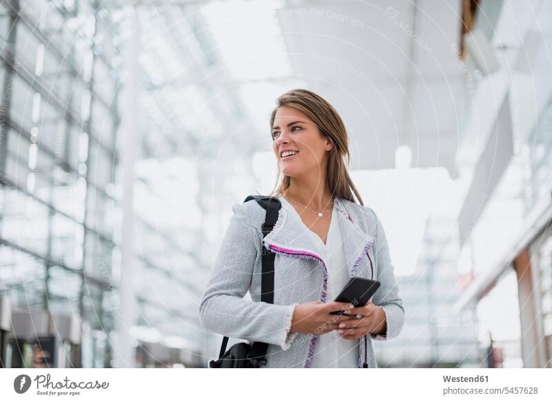 Portrait of smiling young businesswoman with cell phone at the airport looking around mobile phone mobiles mobile phones Cellphone cell phones looking round