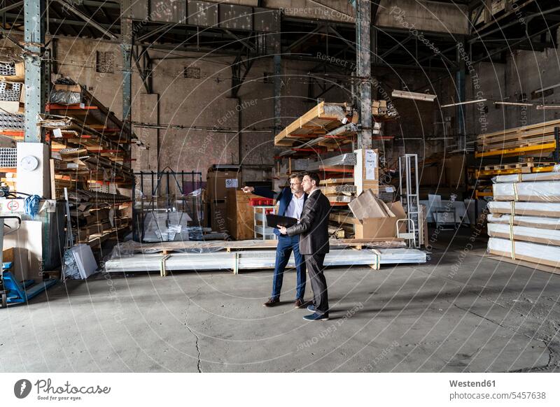 Two businessmen with folder talking in an old storehouse speaking storage warehouse file folders portfolio portfolios files dumps stock Germany executive