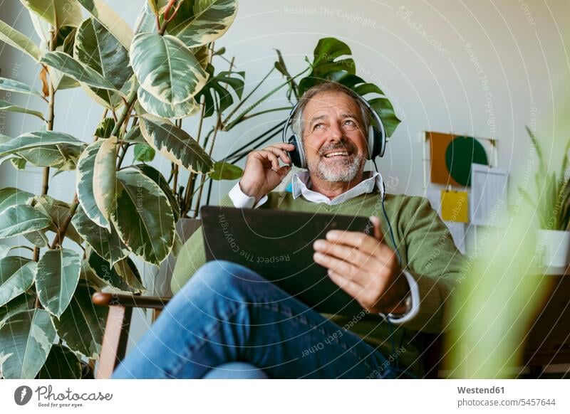 Mature men with digital tablet looking away while listening music at home color image colour image indoors indoor shot indoor shots interior interior view