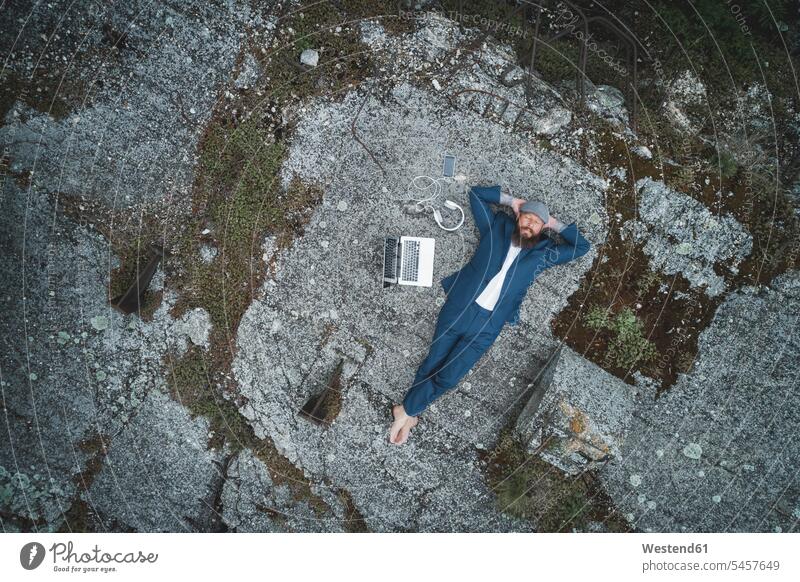 Aerial view of businessman wearing suit with hands behind head relaxing on land in forest color image colour image Austria outdoors location shots outdoor shot