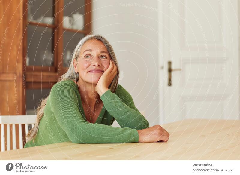 Smiling woman day dreaming while sitting by table at home Germany indoors indoor shot indoor shots interior interior view Interiors daylight shot daylight shots