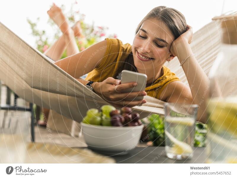 Smiling young woman using mobile phone while resting on hammock color image colour image Germany leisure activity leisure activities free time leisure time