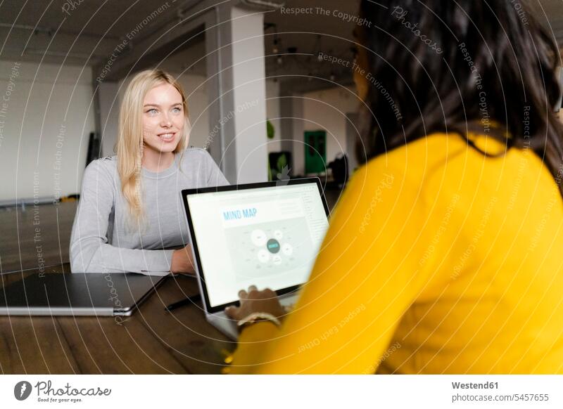 Two young businesswomen with laptop talking at conference table in loft office Conference Table businesswoman business woman business women lofts