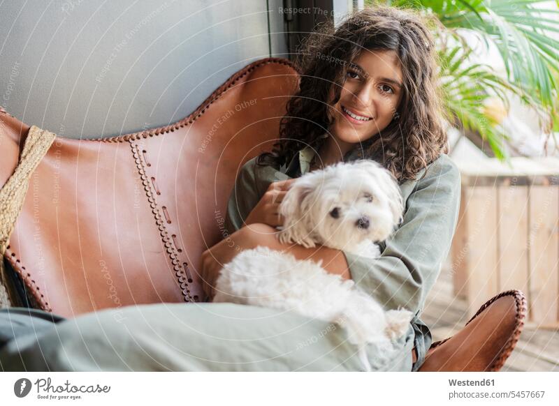 Smiling girl holding puppy while sitting on chair at home color image colour image indoors indoor shot indoor shots interior interior view Interiors day