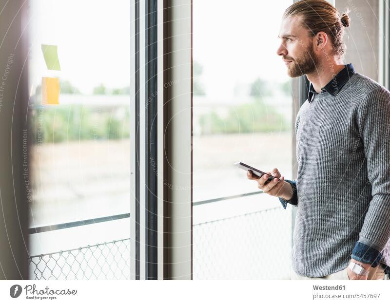 Young businessman with cell phone looking out of window mobile phone mobiles mobile phones Cellphone cell phones confidence confident Businessman Business man