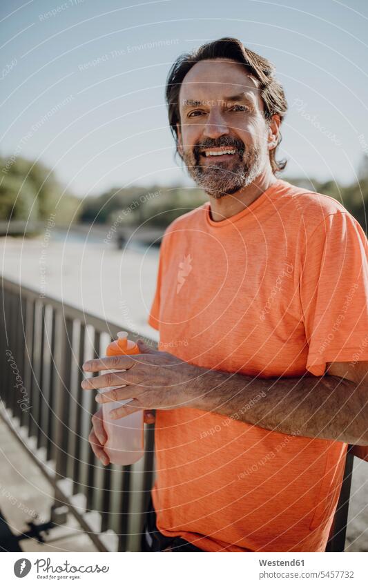 Portrait of smiling man holding water bottle while standing against clear sky in park color image colour image Germany outdoors location shots outdoor shot