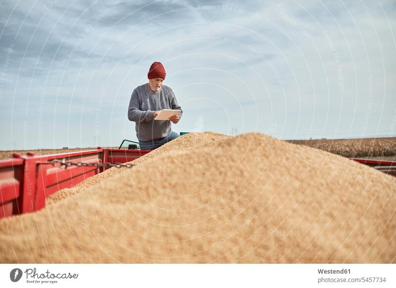 Farmer using digital tablet while standing on tractor against clear sky color image colour image outdoors location shots outdoor shot outdoor shots day