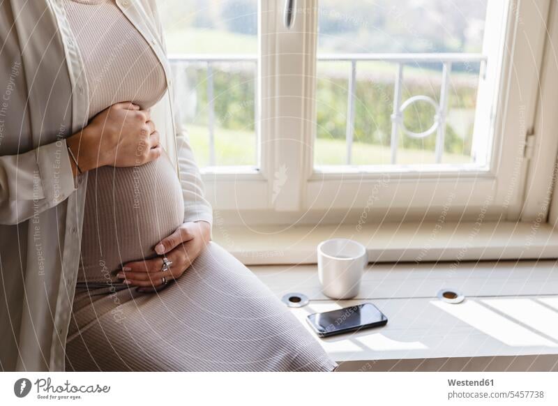 Pregnant woman hands on stomach sitting by window at home color image colour image indoors indoor shot indoor shots interior interior view Interiors day
