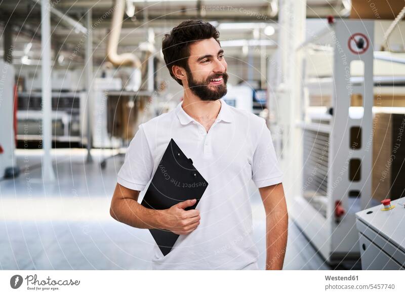 Smiling employee holding clipboard in a factory Occupation Work job jobs profession professional occupation blue collar blue collar worker blue-collar worker