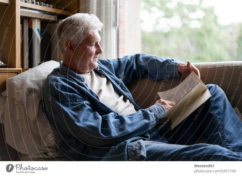Senior man reading book while relaxing on sofa at home color image colour image indoors indoor shot indoor shots interior interior view Interiors day