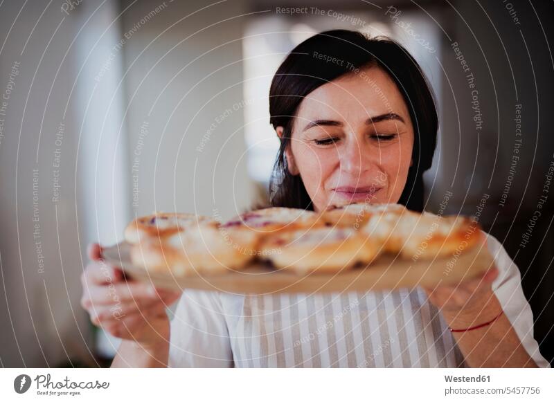 Mature woman serving homemade cakes ona wooden tray bake cook smile smell delight enjoyment Pleasant pleasure happy pleased at home Alimentation food
