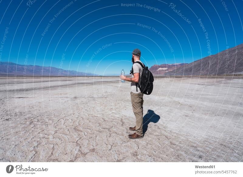 USA, California, Death Valley, man with backpack and water bottle standing in desert looking at distance rucksacks backpacks back-packs Deserts men males