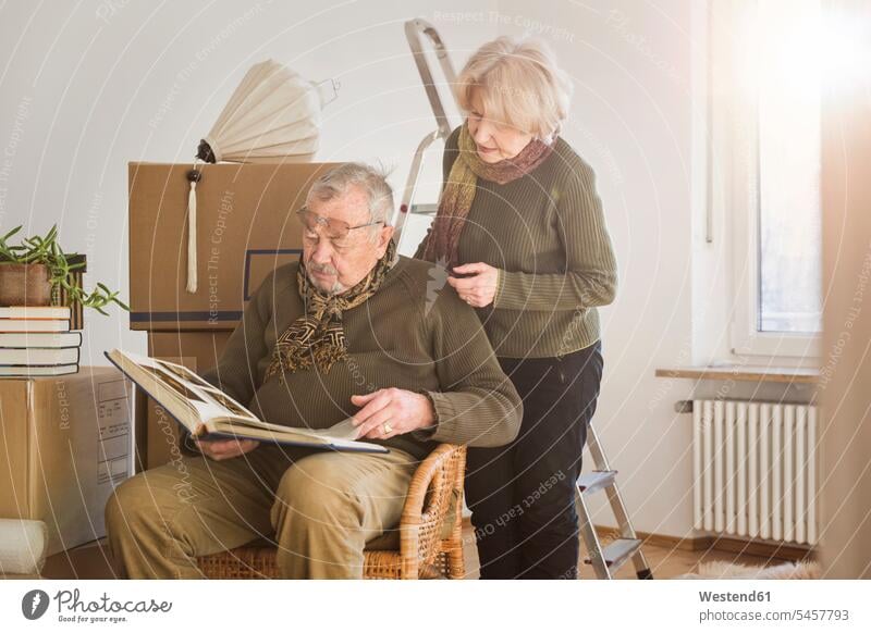 Senior couple looking at photo album surrounded by cardboard boxes in an empty room Cardboard Carton Cardboards cardbox cardboxes carton cartons images picture