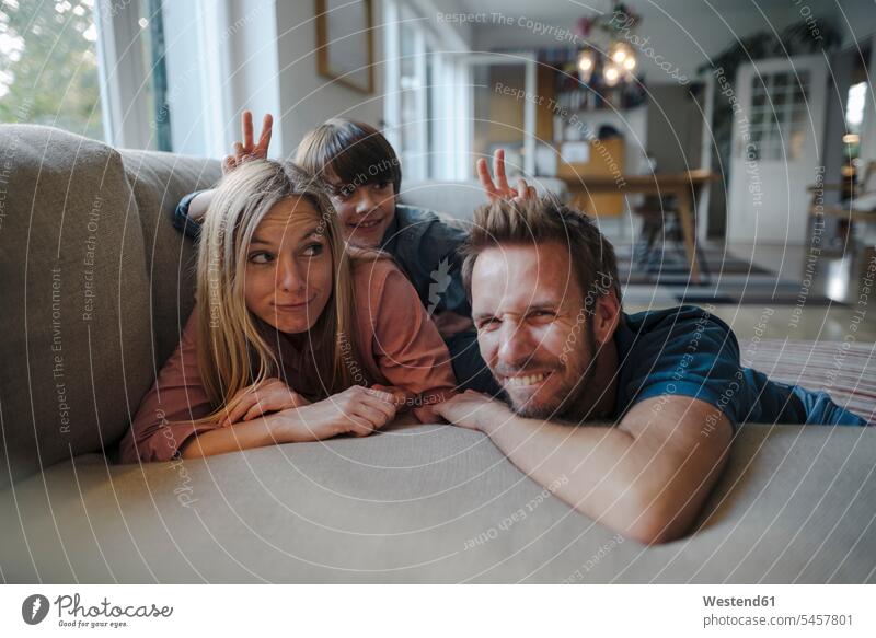 Happy family lying on couch, son making fun of his parents couches settee settees sofa sofas smile Secure happy Emotions Feeling Feelings Sentiment Sentiments