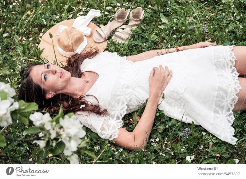 Portrait of daydreaming young woman wearing white lace dress lying on flower meadow portrait portraits females women laying down lie lying down Foral Field