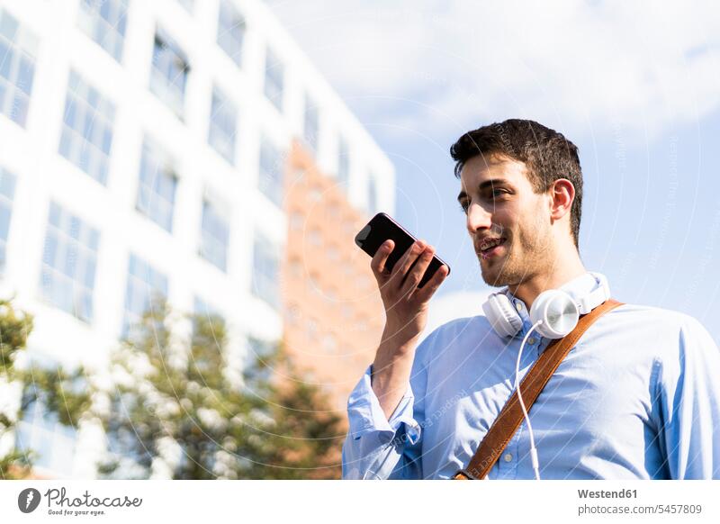 Young man using smartphone, headphones around neck in the city shirts headset telecommunication telephone telephones cell phone cell phones Cellphone mobile