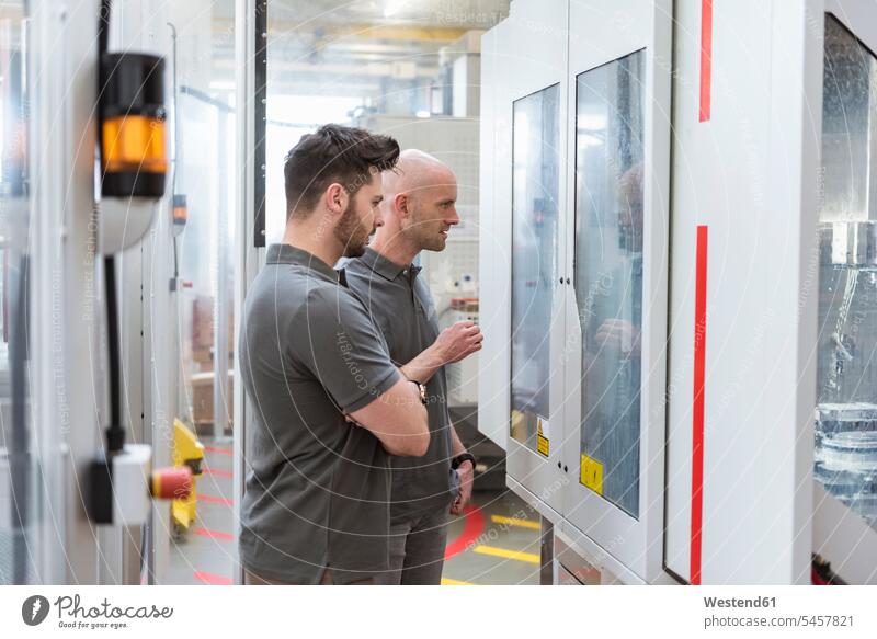 Two men examining machine in modern factory checking examine man males contemporary factories examination examinations Adults grown-ups grownups adult people