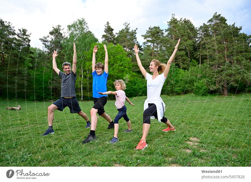 Family practicing warrior poses on grassy land in forest color image colour image Germany wood woods forests nature natural world the natural world outdoors