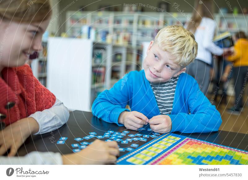 Pupils playing a board game in school library smiling at each other student pupils looking eyeing board-games boardgame board games schools smile schoolchildren