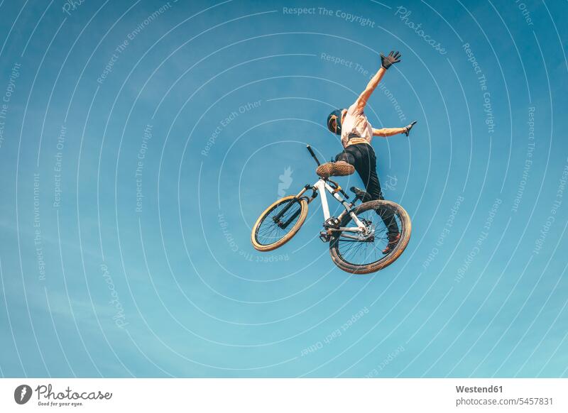 Carefree man performing stunt with bicycle against blue sky during sunset color image colour image Spain leisure activity leisure activities free time